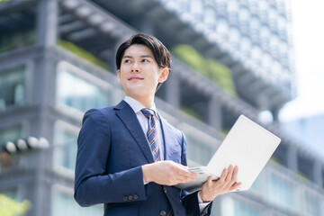 屋外でノートPCを開いて業務するビジネスパーソン